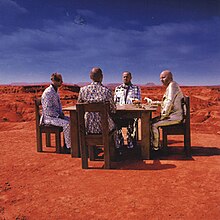 Four men sitting in a table at the Grand Canyon with horses on the table and the earth in the background